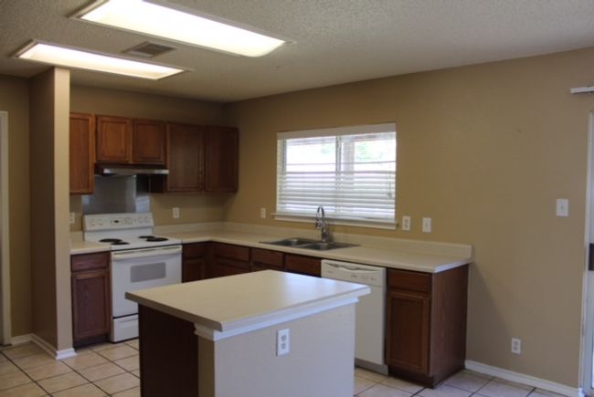 Kitchen with white appliances, a sink, under cabinet range hood, light tile patterned flooring, and light countertops | Image 4