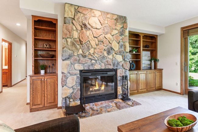 Inviting lower-level living area with floor-to-ceiling stone fireplace and custom oak entertainment center. | Image 21