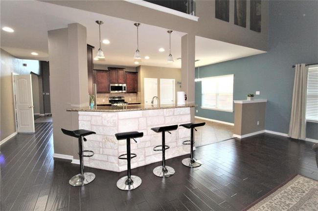 Kitchen with stainless steel appliances, dark wood finished floors, a breakfast bar area, light stone countertops, and hanging light fixtures | Image 12