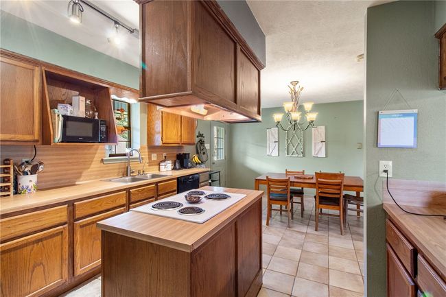 Kitchen featuring black appliances, brown cabinets, decorative light fixtures, a kitchen island, and a chandelier | Image 10