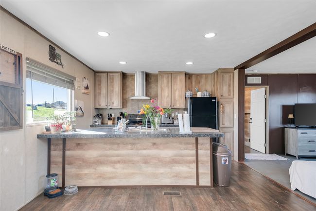 Kitchen featuring visible vents, a sink, dark wood finished floors, freestanding refrigerator, and wall chimney range hood | Image 16