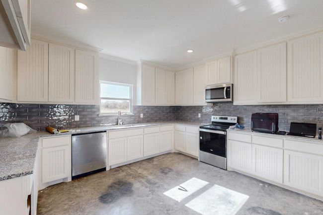 Kitchen with concrete floors, a sink, light stone countertops, decorative backsplash, and stainless steel appliances | Image 15