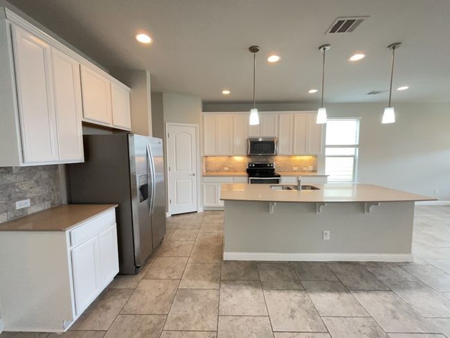 Kitchen featuring appliances with stainless steel finishes, decorative backsplash, white cabinets, recessed lighting, and an island with sink | Image 5