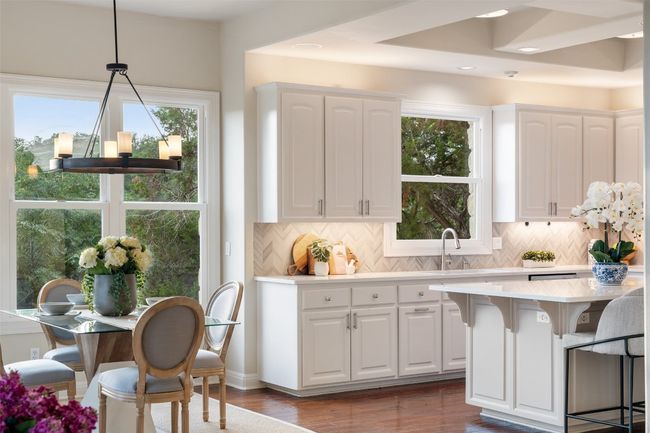 Kitchen with a breakfast bar area, light countertops, backsplash, white cabinetry, and dark wood-type flooring | Image 14