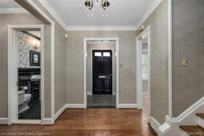 Foyer with dark wood finished floors, a chandelier, crown molding, wallpapered walls, and tile walls | Image 11