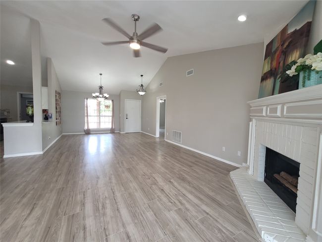 Unfurnished living room with ceiling fan, a fireplace, vaulted ceiling, light wood-style flooring, and baseboards | Image 4