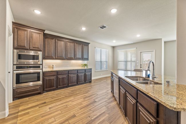 Kitchen with stainless steel appliances, light wood-style floors, dark brown wood cabinetry, recessed lighting, and granite countertops | Image 6