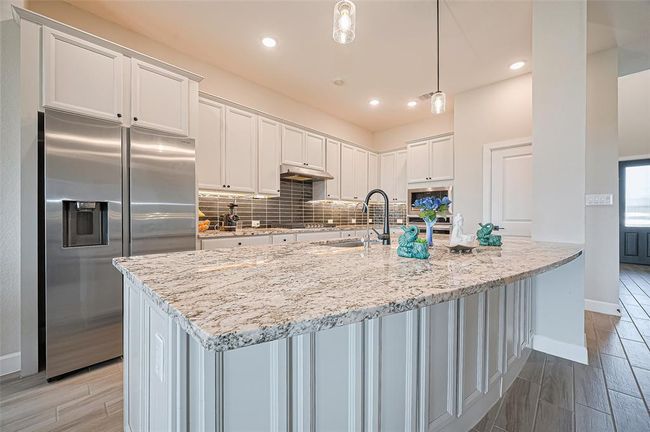 Oversized granite island with a deep sink and pendant lighting, ideal for prepping meals or casual dining—centrally located in this open-concept layout. | Image 11
