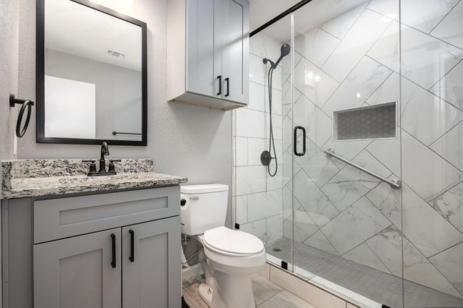 Bathroom featuring a stall shower, vanity, toilet, a textured wall, and marble look tile flooring | Image 30