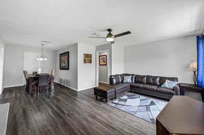 This is a spacious and well-lit open-plan living and dining area featuring contemporary dark wood flooring, neutral wall colors, and modern fixtures. The space is versatile for relaxation and dining, complete with ceiling fans for comfort. | Image 2