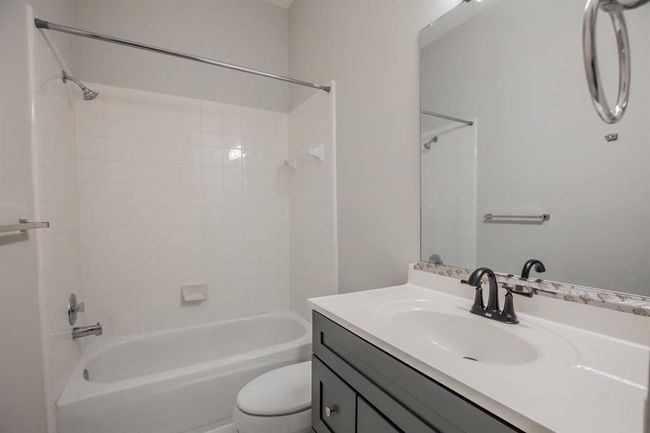 This bathroom features a clean and modern design with a white bathtub-shower combo, a sleek vanity with a dark faucet, and neutral tile walls, providing a bright and functional space. | Image 33