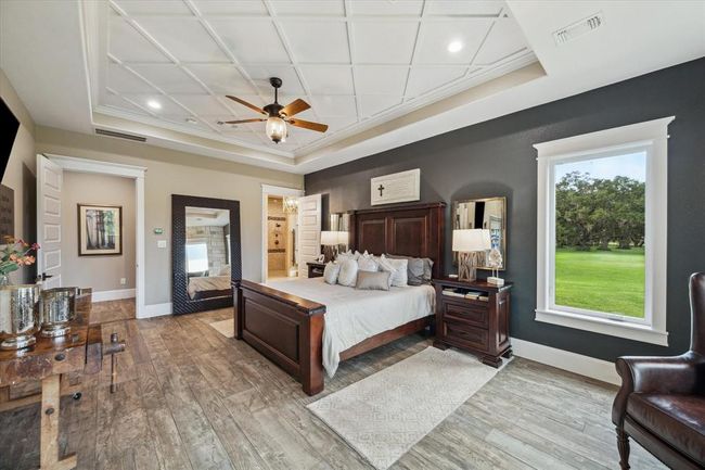 The oversized primary bedroom offers a spacious sitting area, creating a perfect retreat within the home. Four picture windows, framed with custom crown molding, fill the room with natural light and provide beautiful views. A private door leads to the rear covered patio, seamlessly extending the living space outdoors. | Image 17