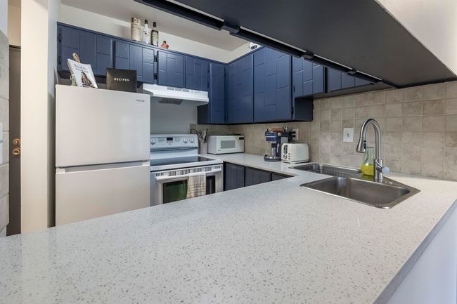 Kitchen featuring white appliances, blue cabinetry, under cabinet range hood, decorative backsplash, and a sink | Image 12