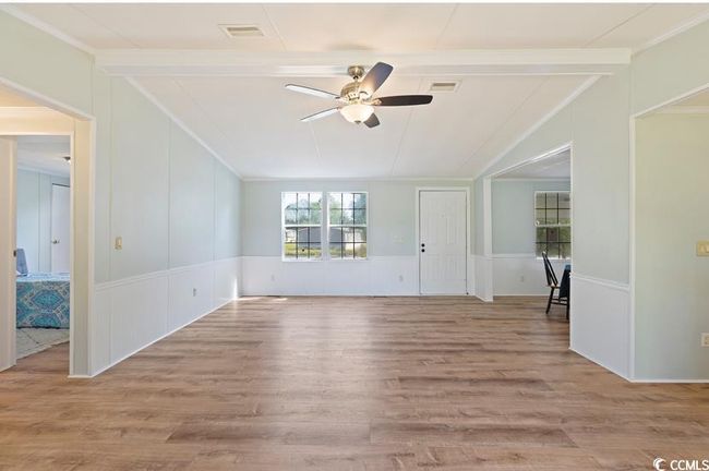 Unfurnished living room with a ceiling fan, a decorative wall, ornamental molding, wood finished floors, and a wainscoted wall | Image 11