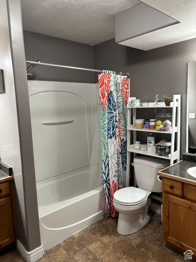 Full bath with vanity, a textured ceiling, toilet, stone finish flooring, and shower / bath combo with shower curtain | Image 14