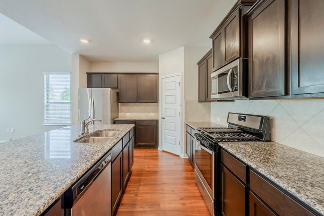 Kitchen featuring wood finished floors, dark brown cabinets, light stone counters, a sink, and appliances with stainless steel finishes | Image 7