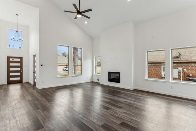 Unfurnished living room with high vaulted ceiling, a chandelier, a ceiling fan, dark wood-style flooring, and a glass covered fireplace | Image 13