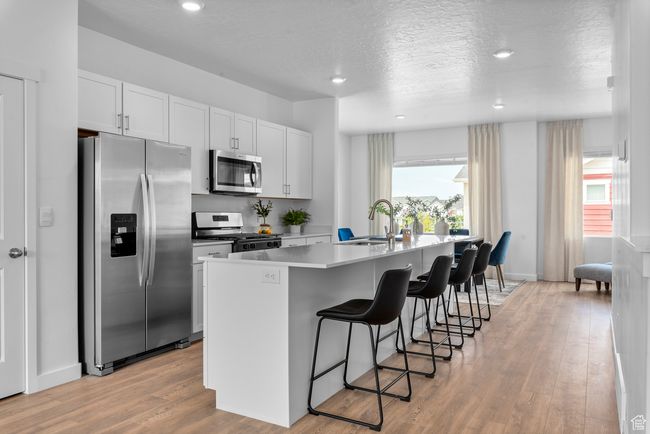 Kitchen with stainless steel appliances, a kitchen breakfast bar, a kitchen island with sink, light wood-style floors, and white cabinets | Image 7