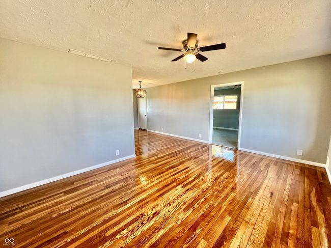 empty room featuring baseboards, a textured ceiling, wood finished floors, and ceiling fan with notable chandelier | Image 4