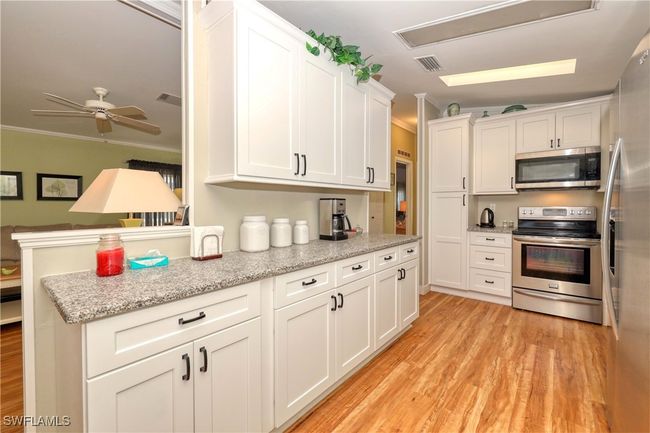 Kitchen with stainless steel appliances, ceiling fan, crown molding, light hardwood / wood-style flooring, and white cabinetry | Image 5