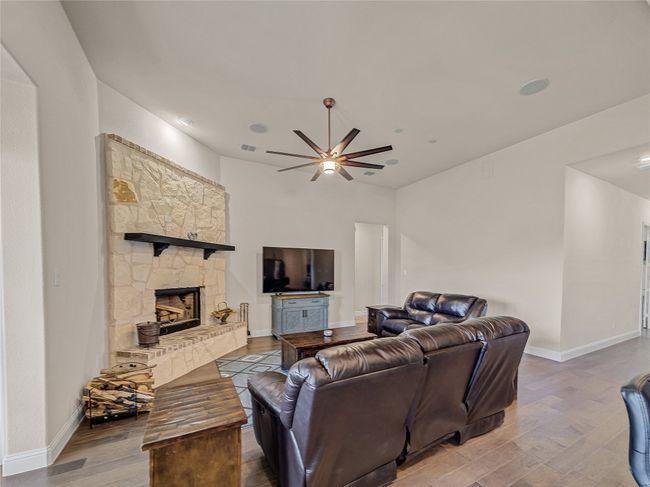 Living area with wood finished floors, a ceiling fan, and a fireplace | Image 15