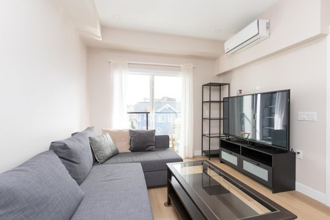 Living area with light wood-style flooring, a wall mounted AC, and baseboards | Image 7