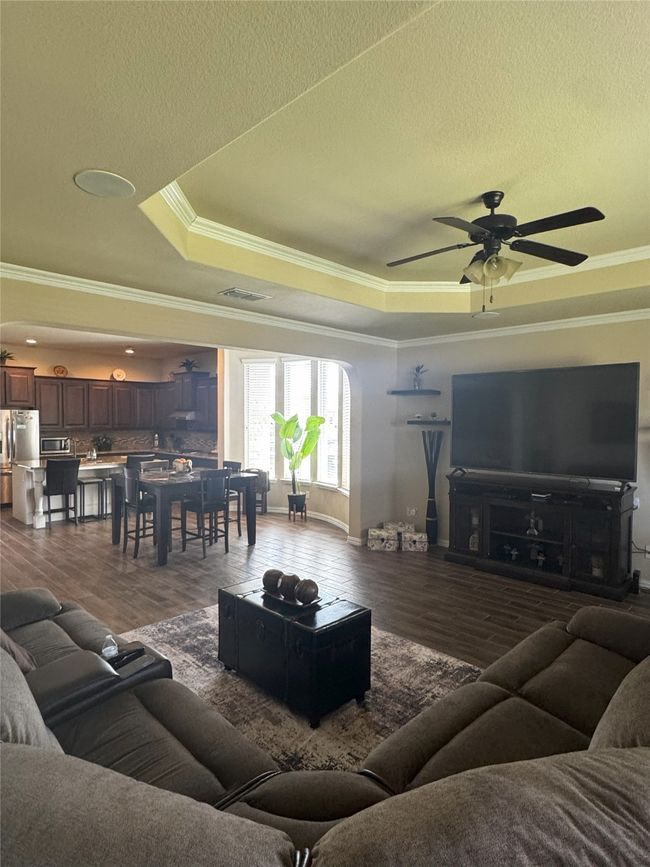 Living area featuring crown molding, a tray ceiling, dark wood-type flooring, a ceiling fan, and a textured ceiling | Image 22