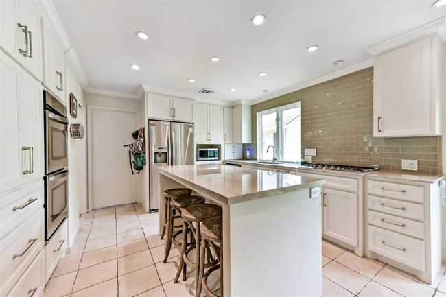 This modern kitchen features sleek white cabinetry, stainless steel appliances, and a stylish tile backsplash. | Image 18