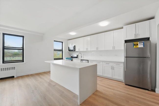Kitchen with white cabinets, light countertops, radiator heating unit, and stainless steel appliances | Image 4