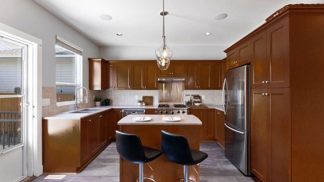 Kitchen with stainless steel appliances, under cabinet range hood, light countertops, a kitchen island, and a sink | Image 11