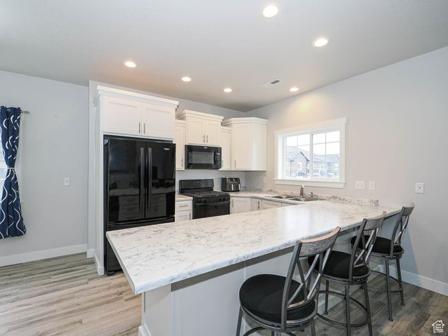 Kitchen with white cabinets, black appliances, a kitchen breakfast bar, and a peninsula | Image 12