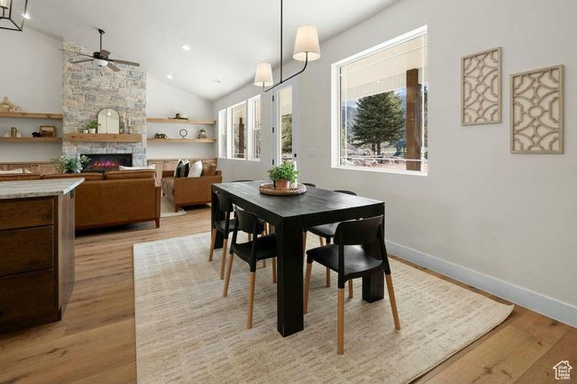 Dining room featuring a stone fireplace, light wood-type flooring, baseboards, high vaulted ceiling, and ceiling fan | Image 12