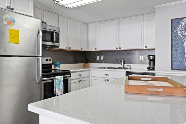 Kitchen featuring decorative backsplash, light stone countertops, stainless steel appliances, white cabinetry, and a sink | Image 20