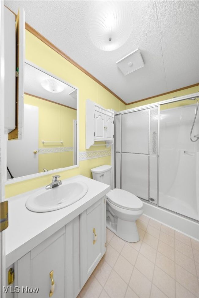 Bathroom featuring a shower stall, vanity, toilet, a textured ceiling, and tile patterned flooring | Image 13