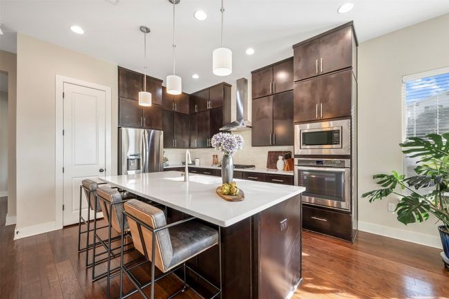 Kitchen featuring appliances with stainless steel finishes, wall chimney range hood, light countertops, dark wood-style flooring, and backsplash | Image 23
