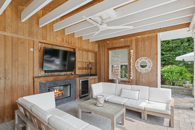 Living area with wooden walls, a glass covered fireplace, ceiling fan, wine cooler, and beam ceiling | Image 26