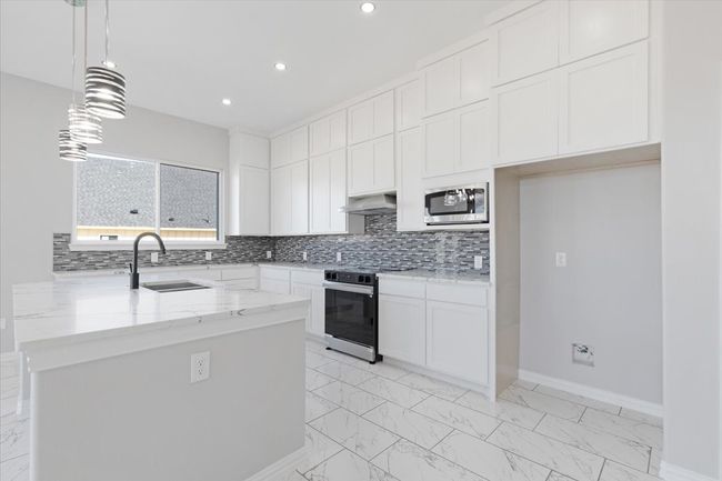 Kitchen featuring range with electric cooktop, light marble finish floors, stainless steel microwave, light stone counters, and recessed lighting | Image 12