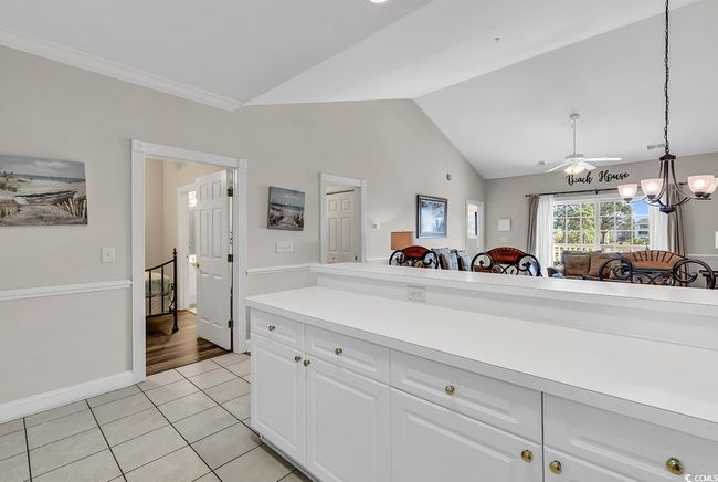 Kitchen featuring vaulted ceiling, light tile patterned floors, light countertops, white cabinets, and hanging light fixtures | Image 6