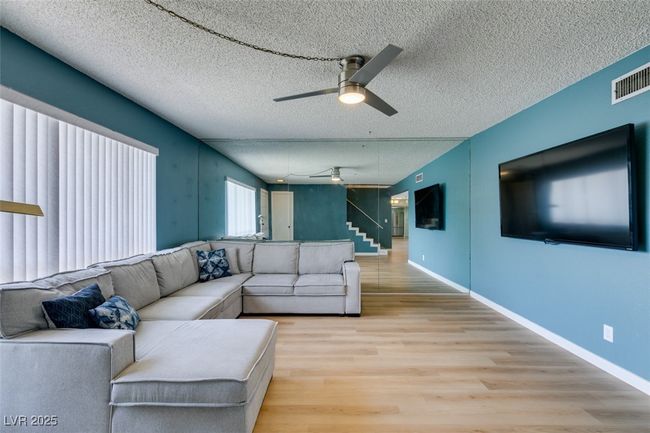Living area featuring a ceiling fan, light wood-style floors, stairs, and a textured ceiling | Image 5