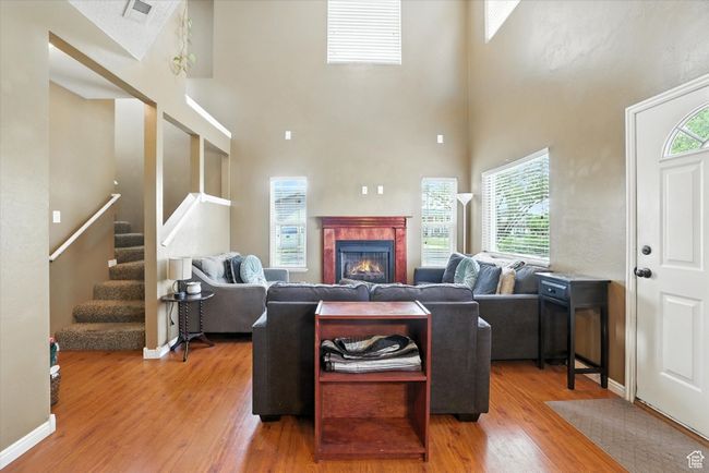 Living area featuring wood finished floors, a towering ceiling, healthy amount of natural light, stairway, and a tiled fireplace | Image 11