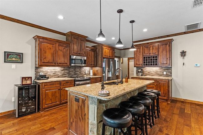 Kitchen featuring hanging light fixtures, stainless steel appliances, a center island with sink, beverage cooler, and hardwood / wood-style flooring | Image 21