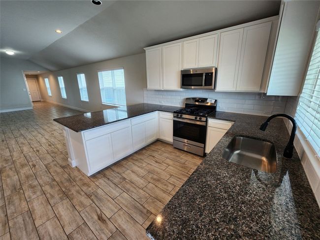Kitchen with appliances with stainless steel finishes, a peninsula, lofted ceiling, light wood-style floors, and white cabinetry | Image 8