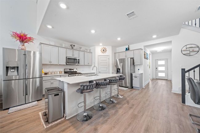 Kitchen featuring a kitchen bar, light wood-type flooring, a sink, light countertops, and stainless steel appliances | Image 9