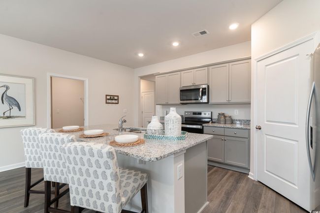 Kitchen featuring stainless steel appliances, gray cabinets, dark wood finished floors, a kitchen breakfast bar, and a kitchen island with sink | Image 9