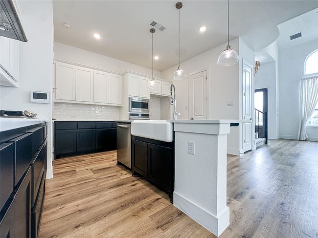 Kitchen with appliances with stainless steel finishes, white cabinets, light wood-type flooring, decorative backsplash, and recessed lighting | Image 11