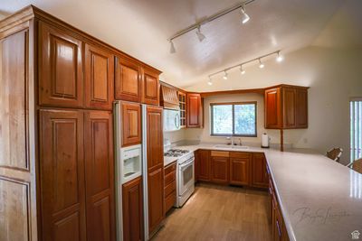 Kitchen featuring sink, white appliances, rail lighting, vaulted ceiling, and light hardwood / wood-style flooring | Image 3