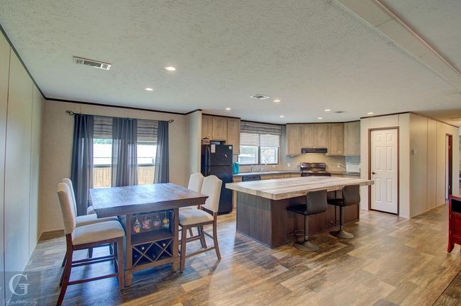 Kitchen with light wood finished floors, a center island, a textured ceiling, black appliances, and under cabinet range hood | Image 5