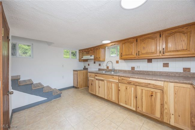Kitchen featuring a sink, a textured ceiling, under cabinet range hood, plenty of natural light, and​​‌​​​​‌​​‌‌​‌‌​​​‌‌​​‌‌​‌​​​​​‌ baseboards | Image 18