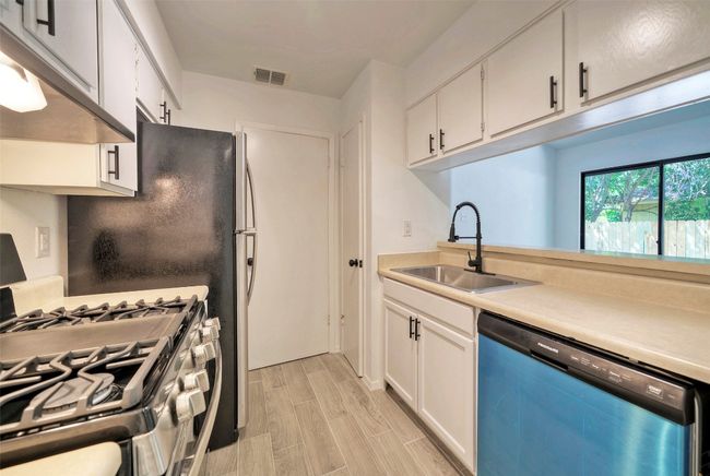 Kitchen featuring dishwasher, stainless steel gas stove, under cabinet range hood, light countertops, and white cabinets | Image 8