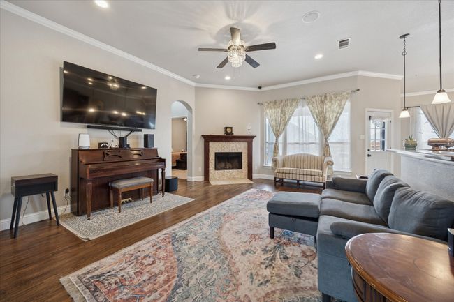 Living area with a ceiling fan, arched walkways, wood finished floors, baseboards, and a tiled fireplace | Image 5